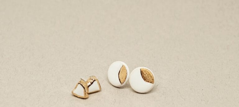 Handmade white ceramic stud earrings with gold accents on a soft beige background