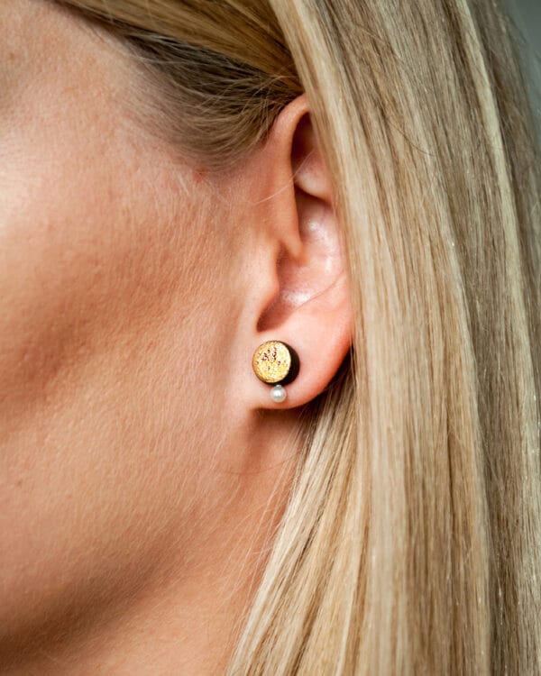 Handmade black earthenware stud earrings with moon-textured surface, gold luster, and a small white pearl