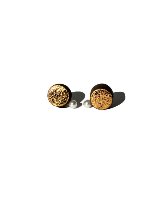 Handmade black earthenware stud earrings with moon-textured surface, gold luster, and a small white pearl