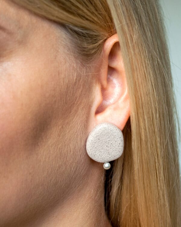 Minimalist ceramic stud earrings in light concrete-colored clay with cracked glaze and a small pearl accent