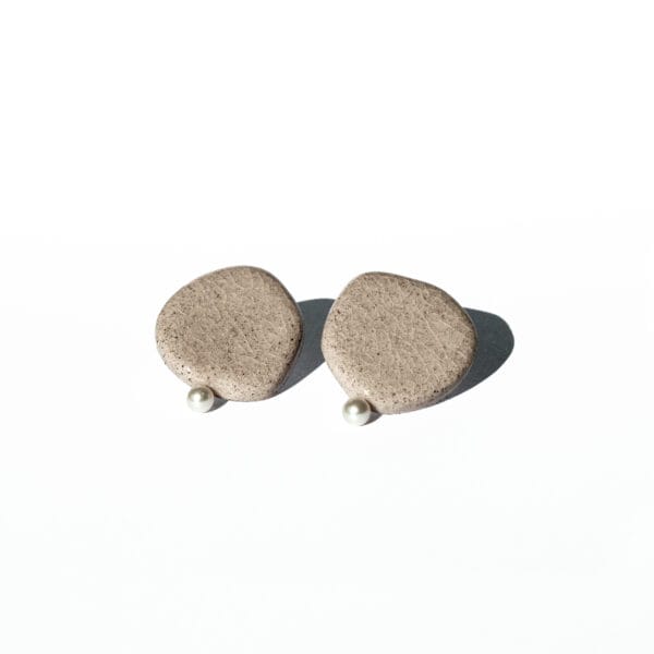 Minimalist ceramic stud earrings in light concrete-colored clay with cracked glaze and a small pearl accent