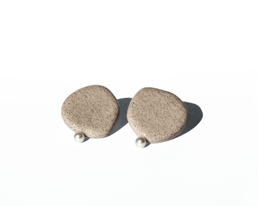 Minimalist ceramic stud earrings in light concrete-colored clay with cracked glaze and a small pearl accent