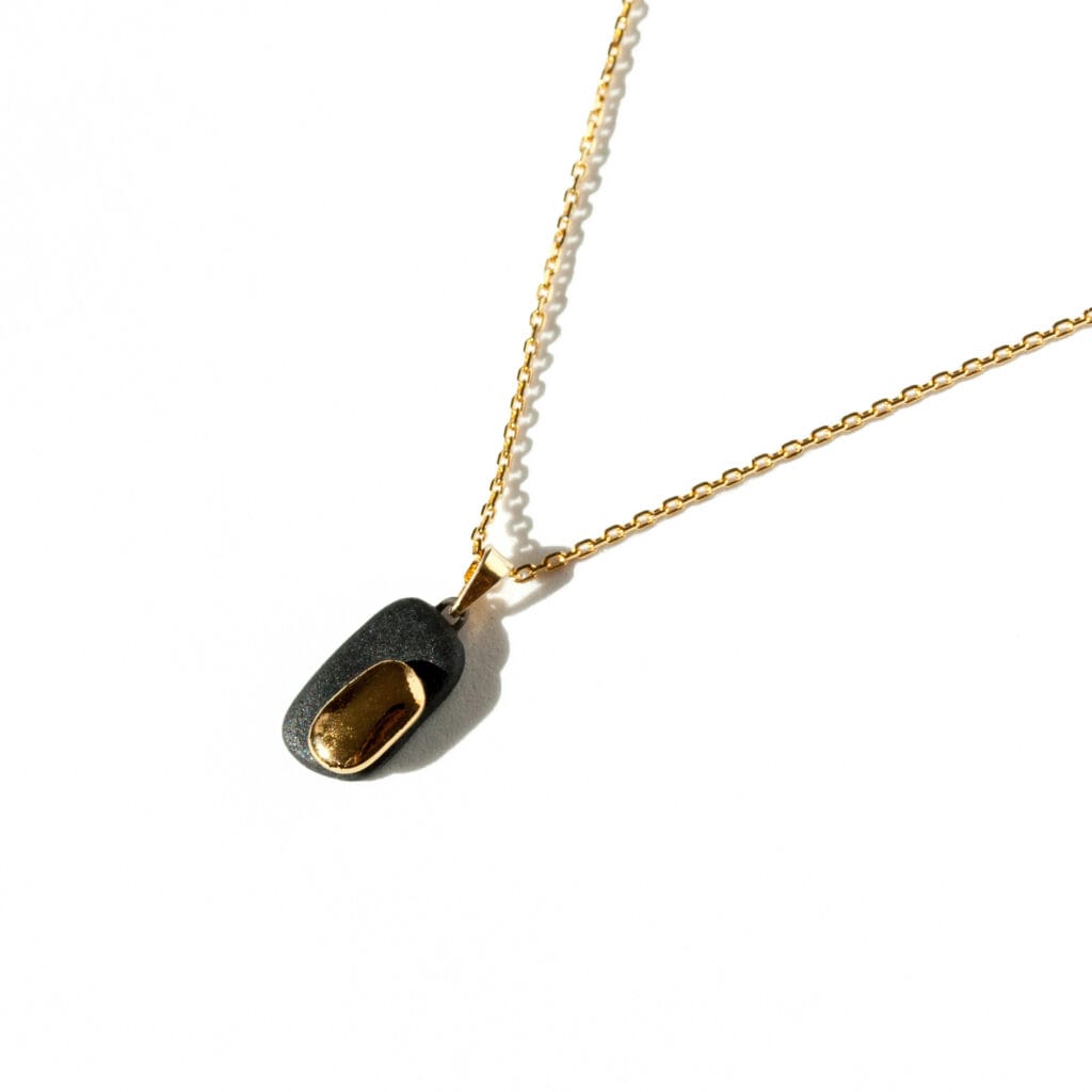 Handmade black porcelain pendant necklace with two-layer design, matte and glossy finishes, gold luster decoration, and gold-plated sterling silver chain and bail
