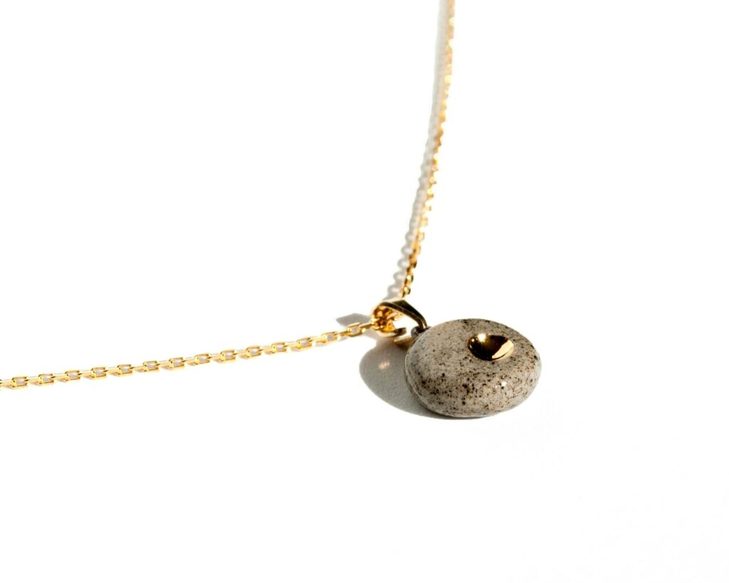 Handmade grey stoneware pendant necklace with black grog, round shape, clear glossy glaze, and hand-painted gold luster detail on gold-plated sterling silver chain