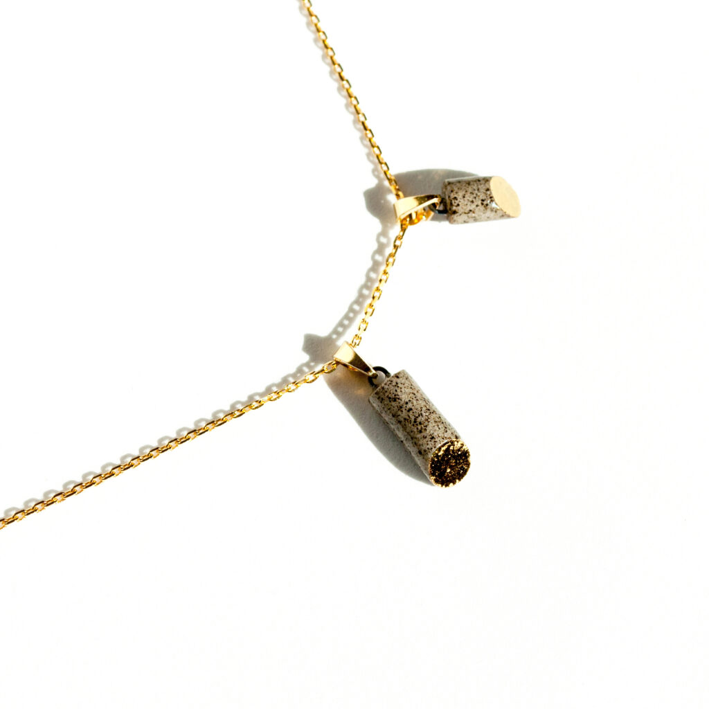 Handmade grey stoneware pipe-shaped pendant with 45-degree oval cut, clear glossy glaze, gold luster detail on the oval, hanging on a gold-plated sterling silver chain.