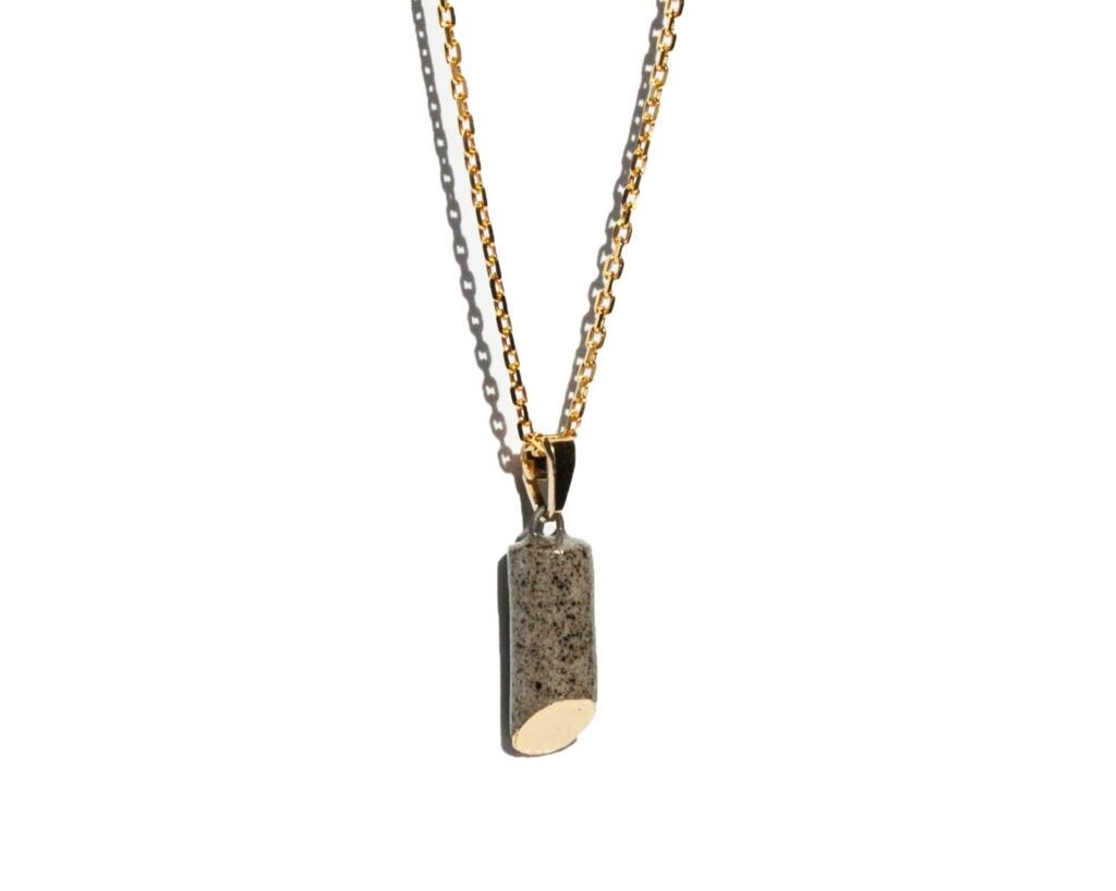 Handmade grey stoneware pipe-shaped pendant with 45-degree oval cut, clear glossy glaze, gold luster detail on the oval, hanging on a gold-plated sterling silver chain.