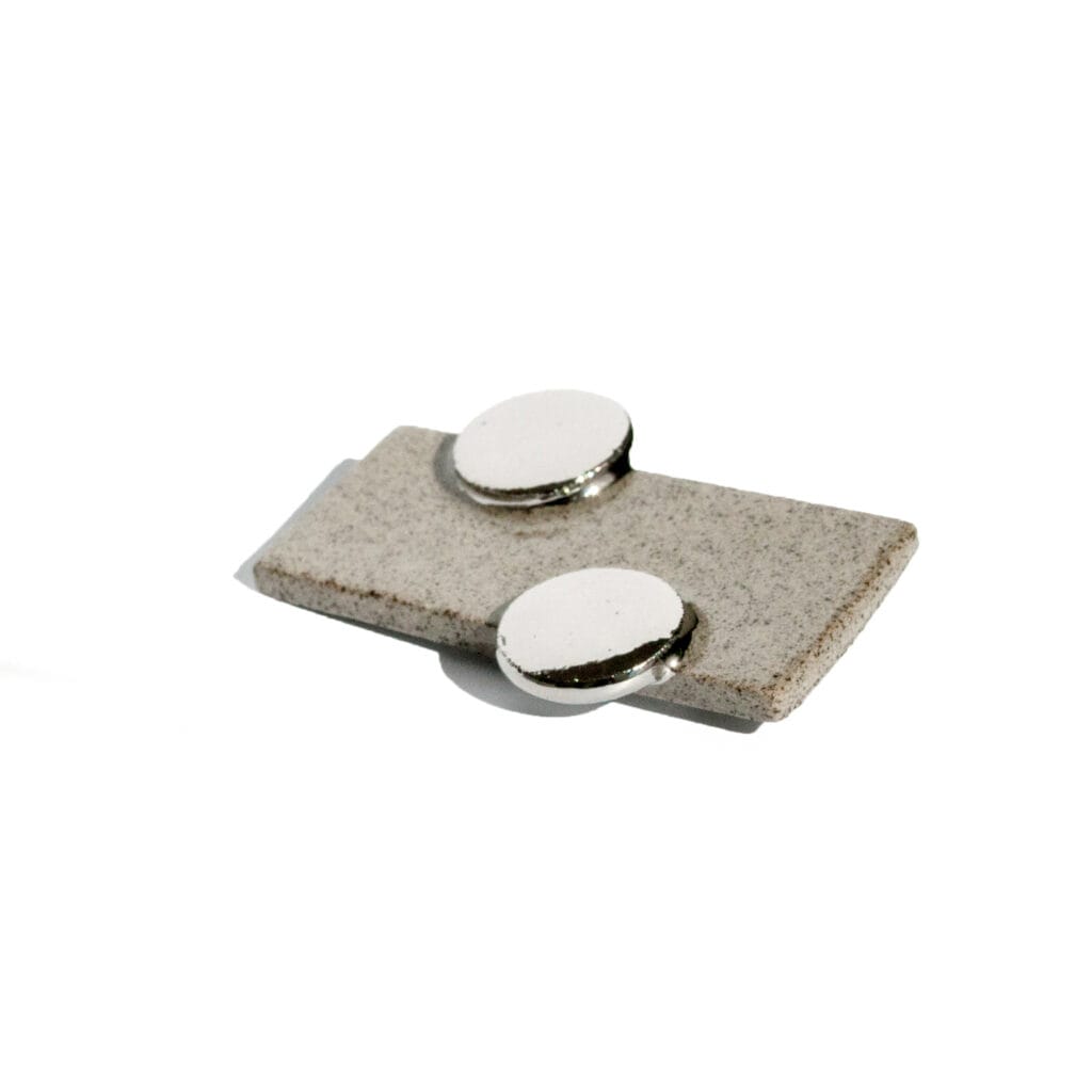 Reflective Balance handmade stoneware brooch with speckled grey rectangular base, glossy glaze, one platinum cylinder on lower left and one on upper right, classic pin back, minimalist geometric design