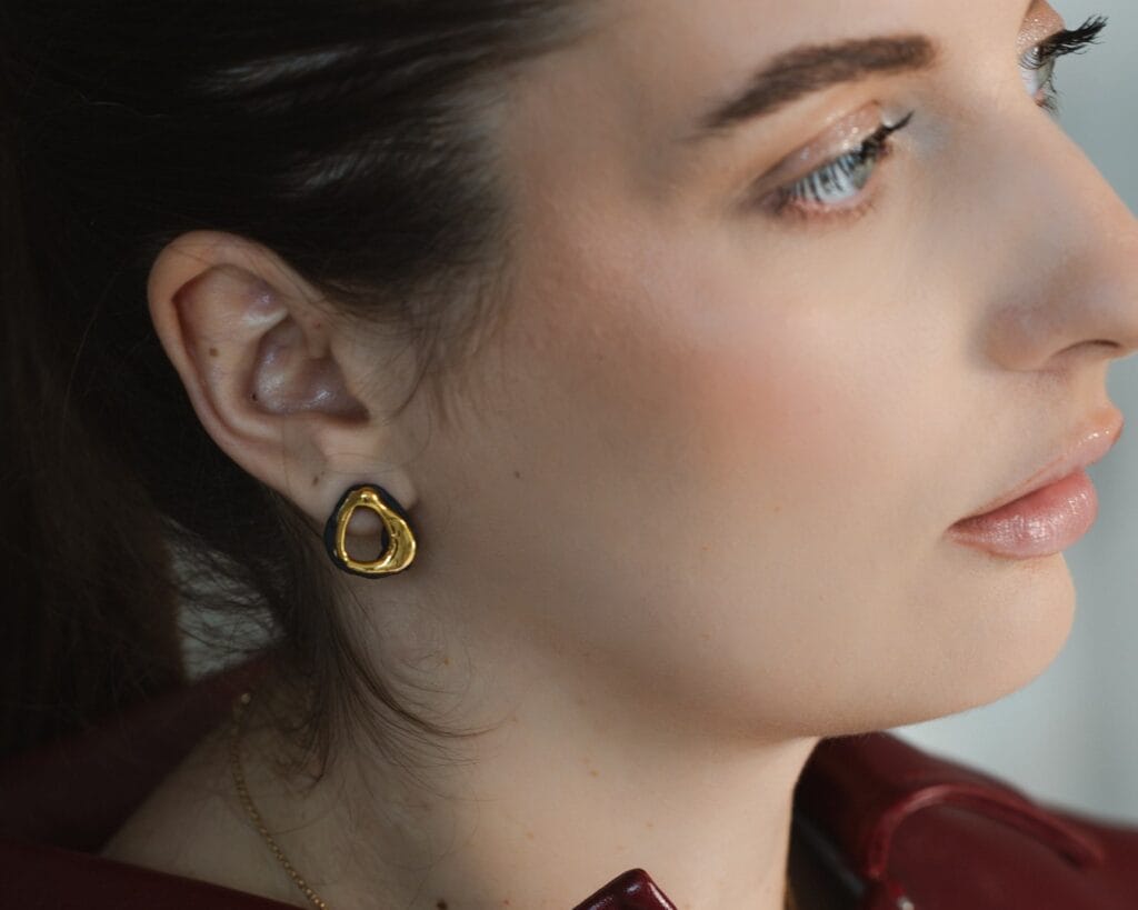 Black Ripple handmade black porcelain earrings with gold detail worn by a model, side profile