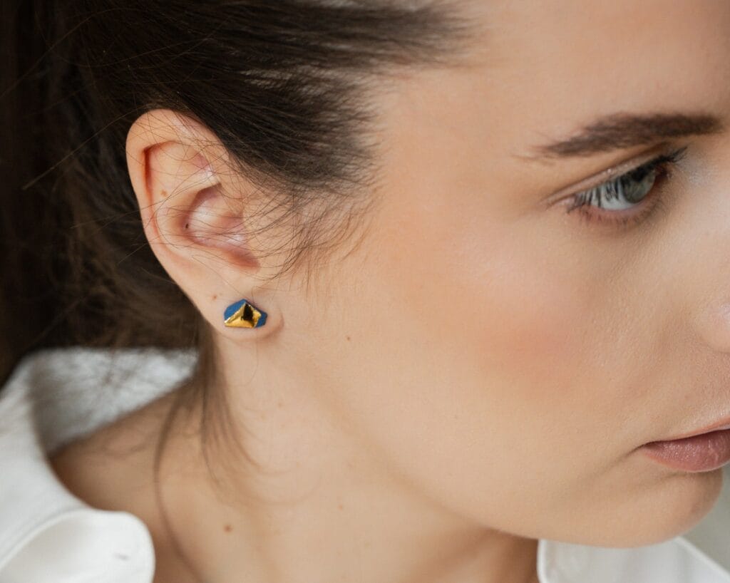 Blue Smithereens Gold handmade blue porcelain earrings with gold luster worn on ear, close-up