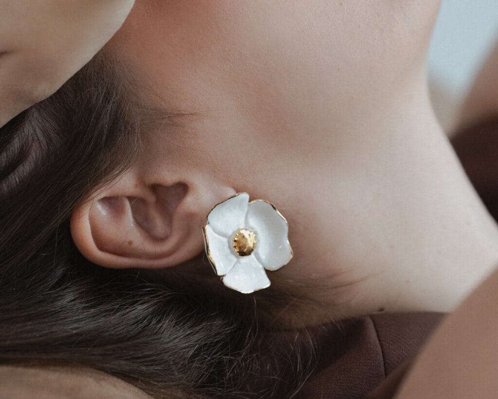White Anemone handmade white porcelain flower earrings with gold center worn on ear, close-up