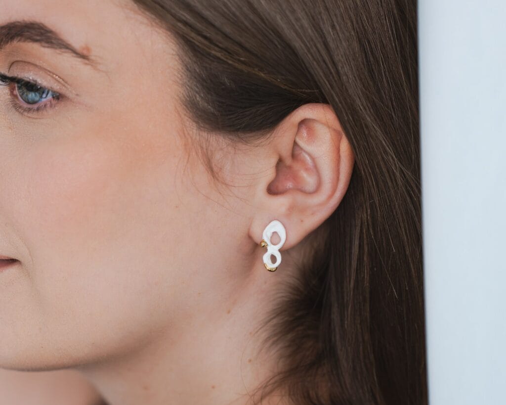 White Infinity handmade white porcelain earrings with gold luster worn by a model, close-up view