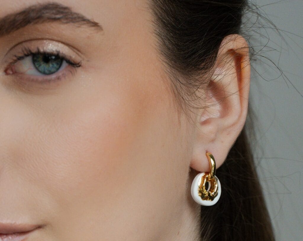 White Loop handmade white porcelain hoop earrings with textured gold detail worn on ear, close-up