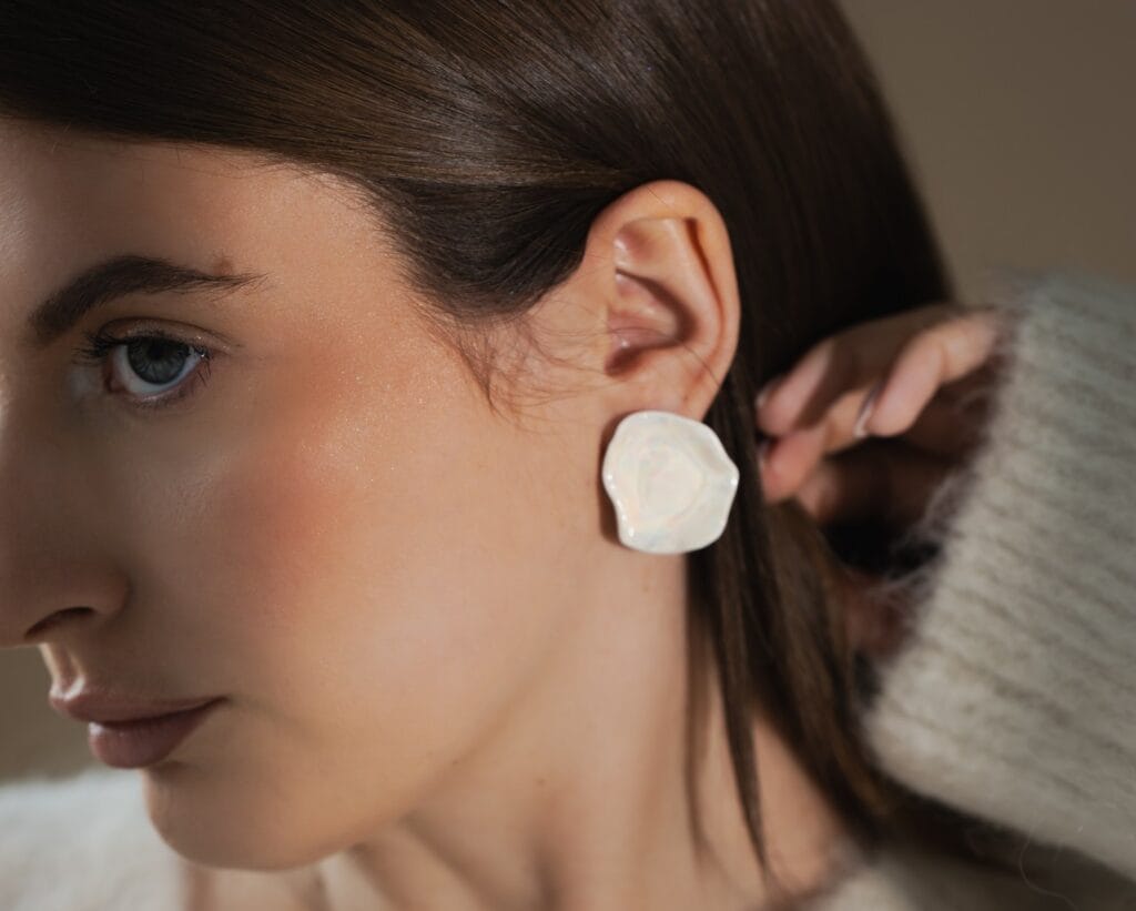 White Matter Large handmade white porcelain earrings with mother of pearl luster worn on ear, portrait view