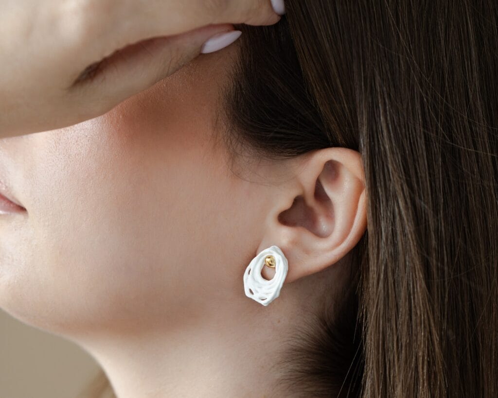 Woven White handmade white porcelain stud earrings with gold detail worn on ear, close-up